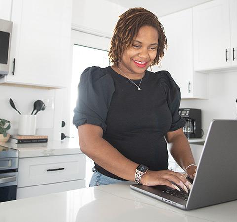 A woman in her kitchen, working on her laptop